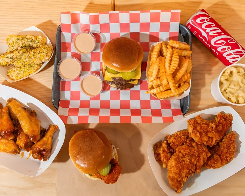 Overhead view of a fast-food meal with burgers, fries, chicken wings, mac and cheese, and corn.