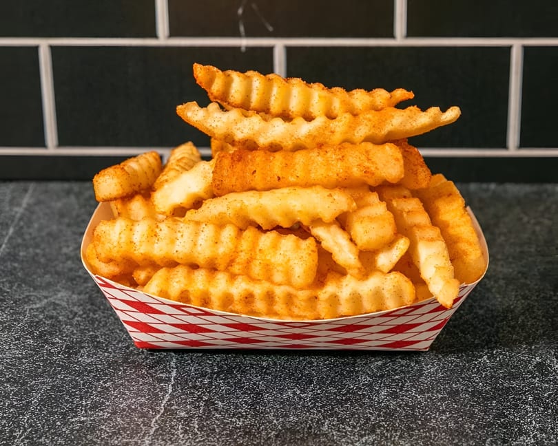 Crinkle-cut fries seasoned with red spices, served in a red and white paper tray.