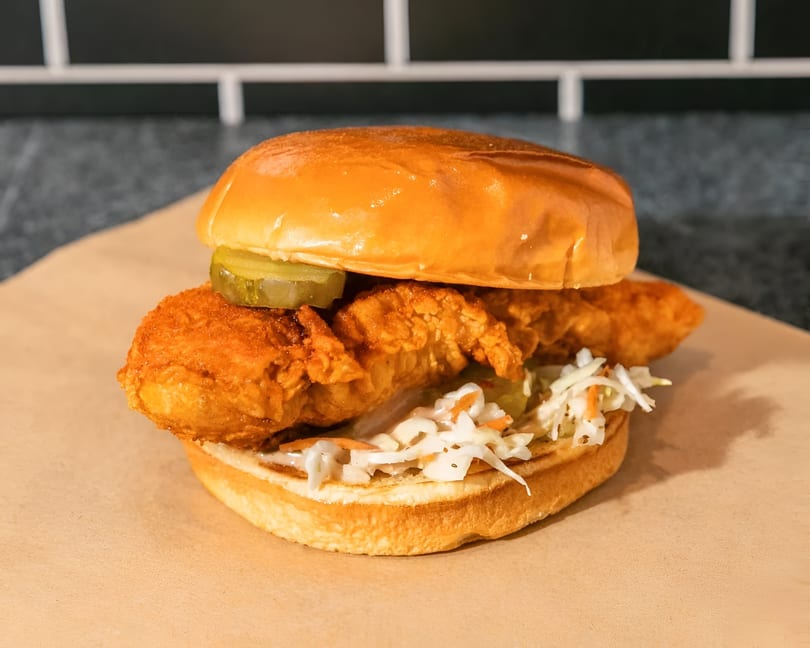 Crispy fried chicken sandwich with pickles and coleslaw on a brioche bun, on a brown paper.