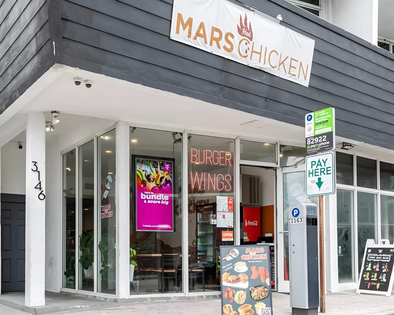 Exterior of Mars Hot Chicken restaurant with a banner, neon signs, and a menu board.